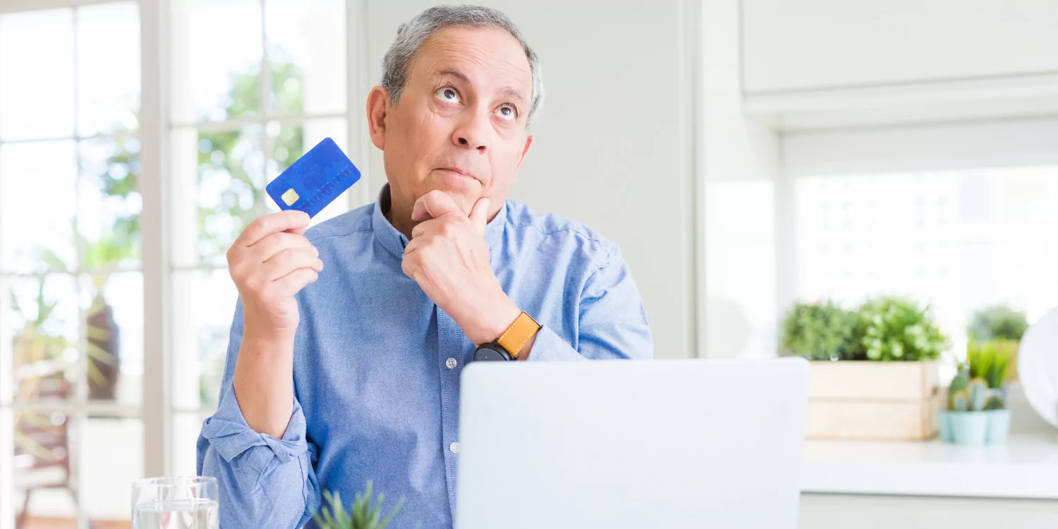 Senior man holding credit card in front of laptop thinking to buy or not to buy - When is the Best Time to Buy a New Furnace?