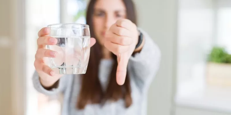 Woman holding glass of water with thumbs down
