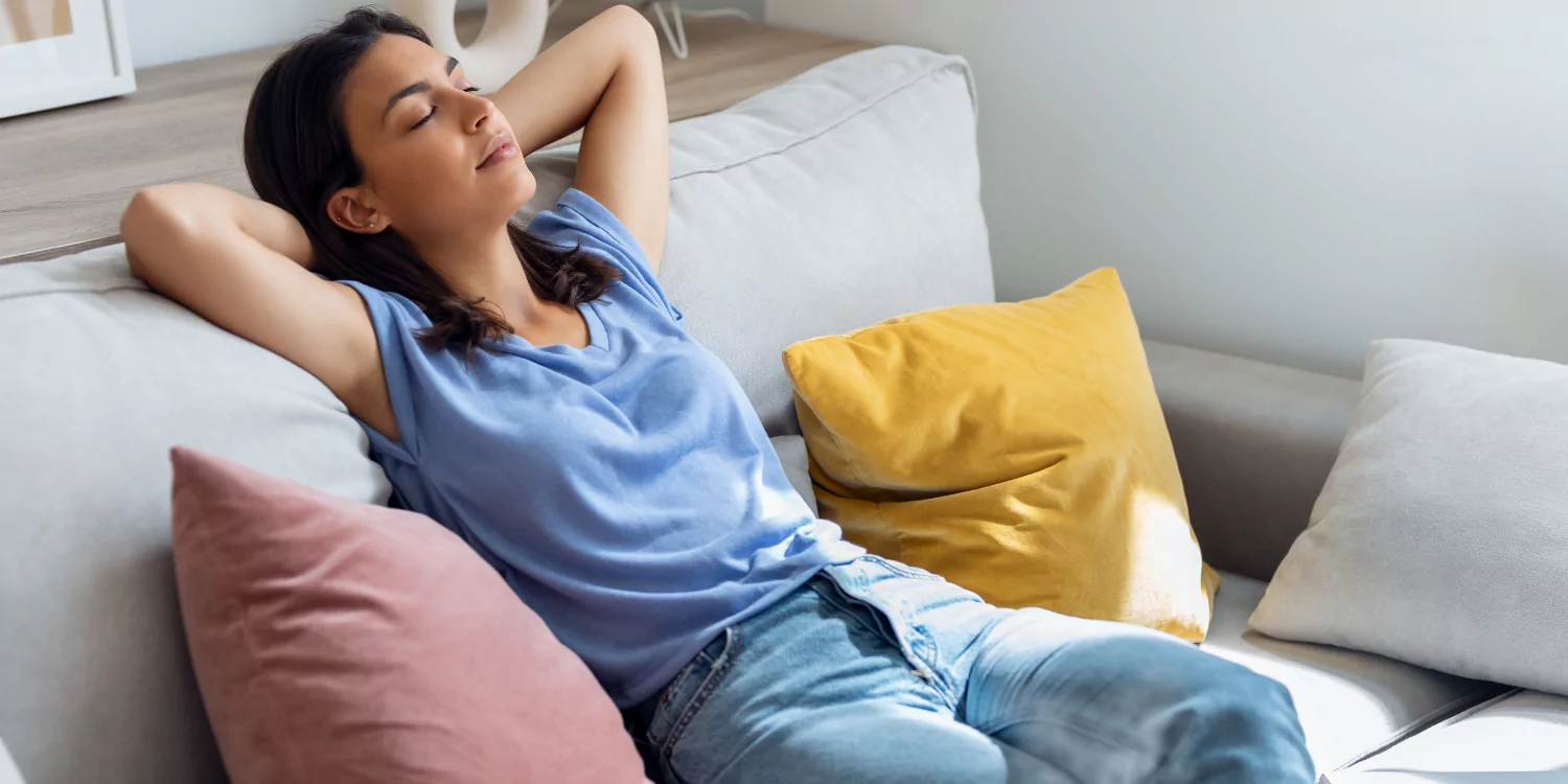 Women sitting on couch breathing in deeply - 4 Ways to Reduce Indoor Air Contaminants in Your Home