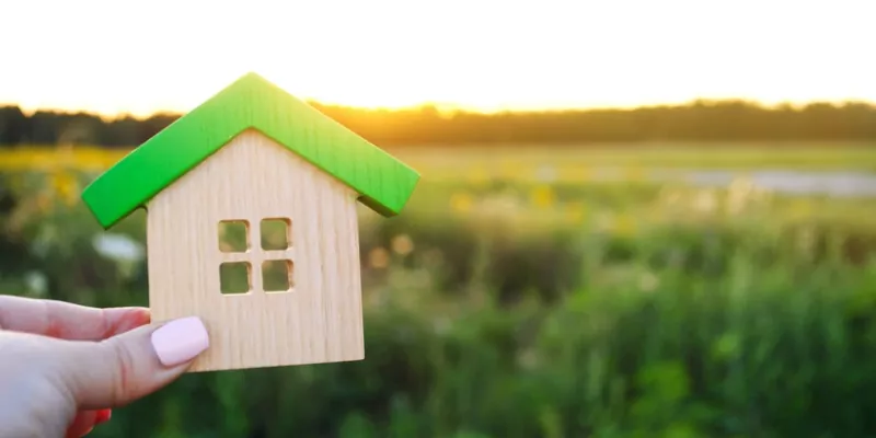Lady holding wooden house against field background