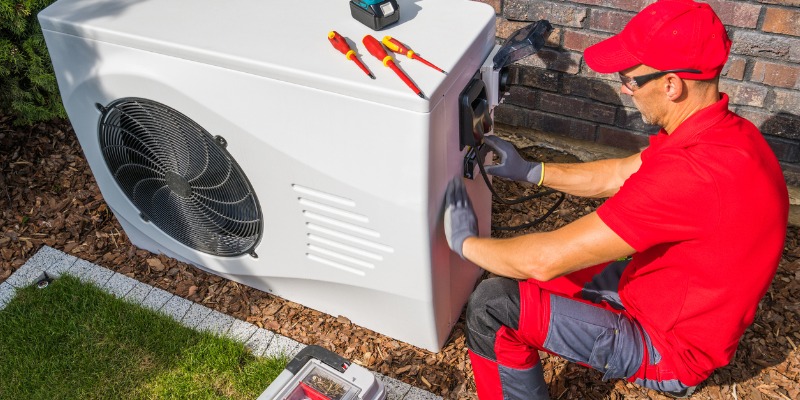 HVAC tech looking at heat pump outdoor unit - Why Is My Geothermal Heating System Making Strange Noises? 